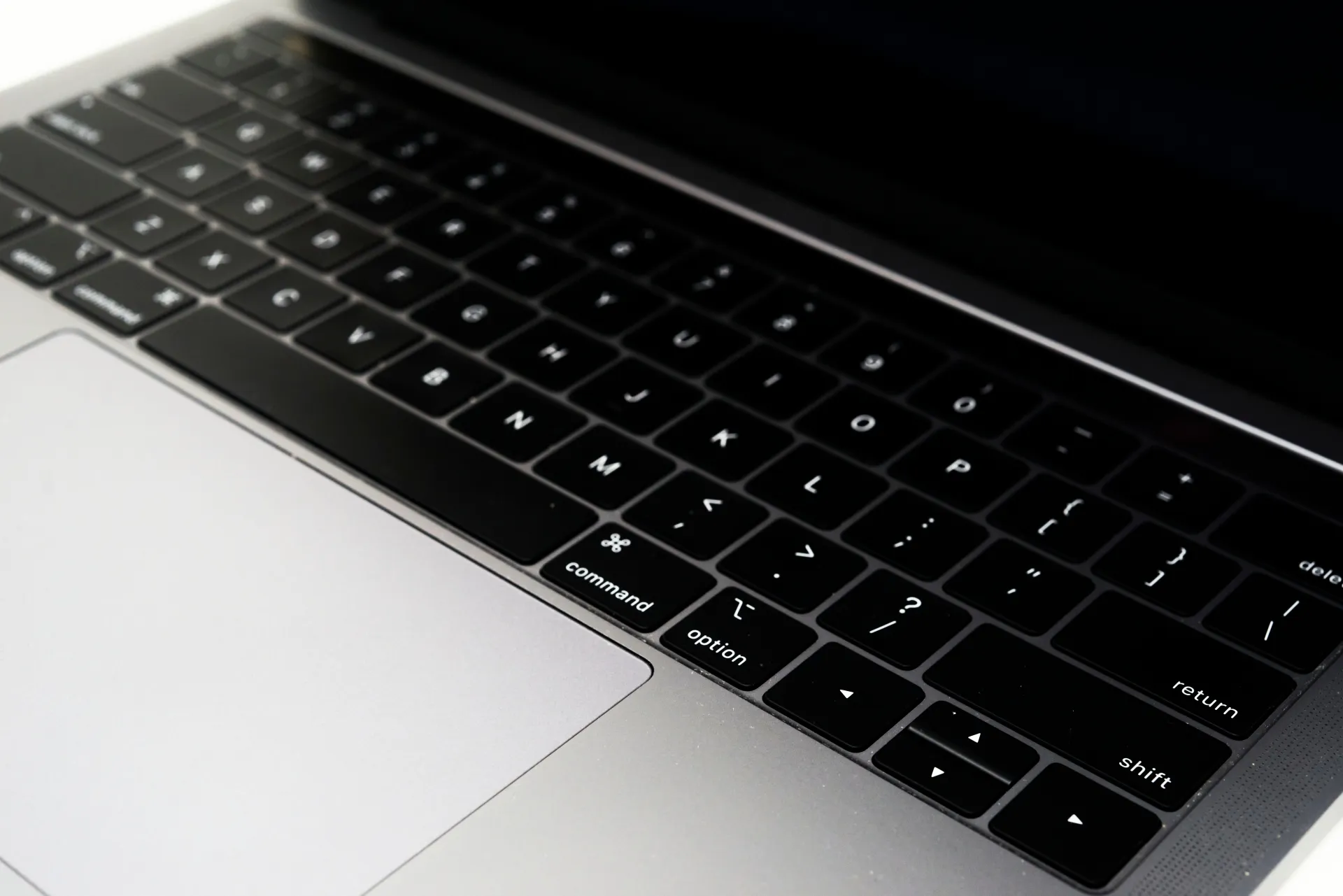 MacBookの英字配列キーボードとトラックパッドを斜めから写した写真(モノクロ)